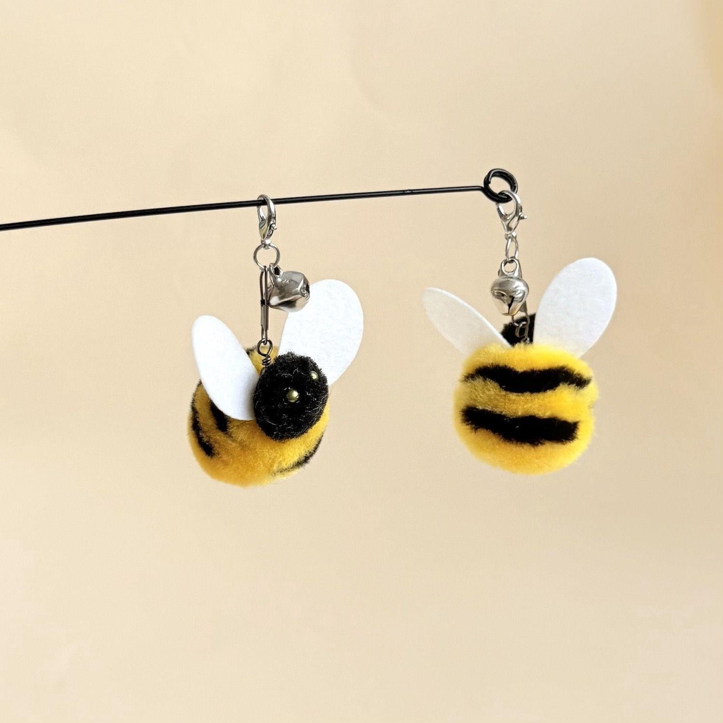 Two yellow-and-black bee cat teaser attachments hanging in front and side views