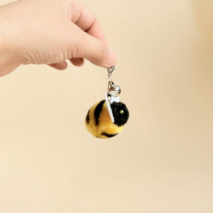 Hand holding a bee cat teaser attachment by its clasp, bell and connecting rings