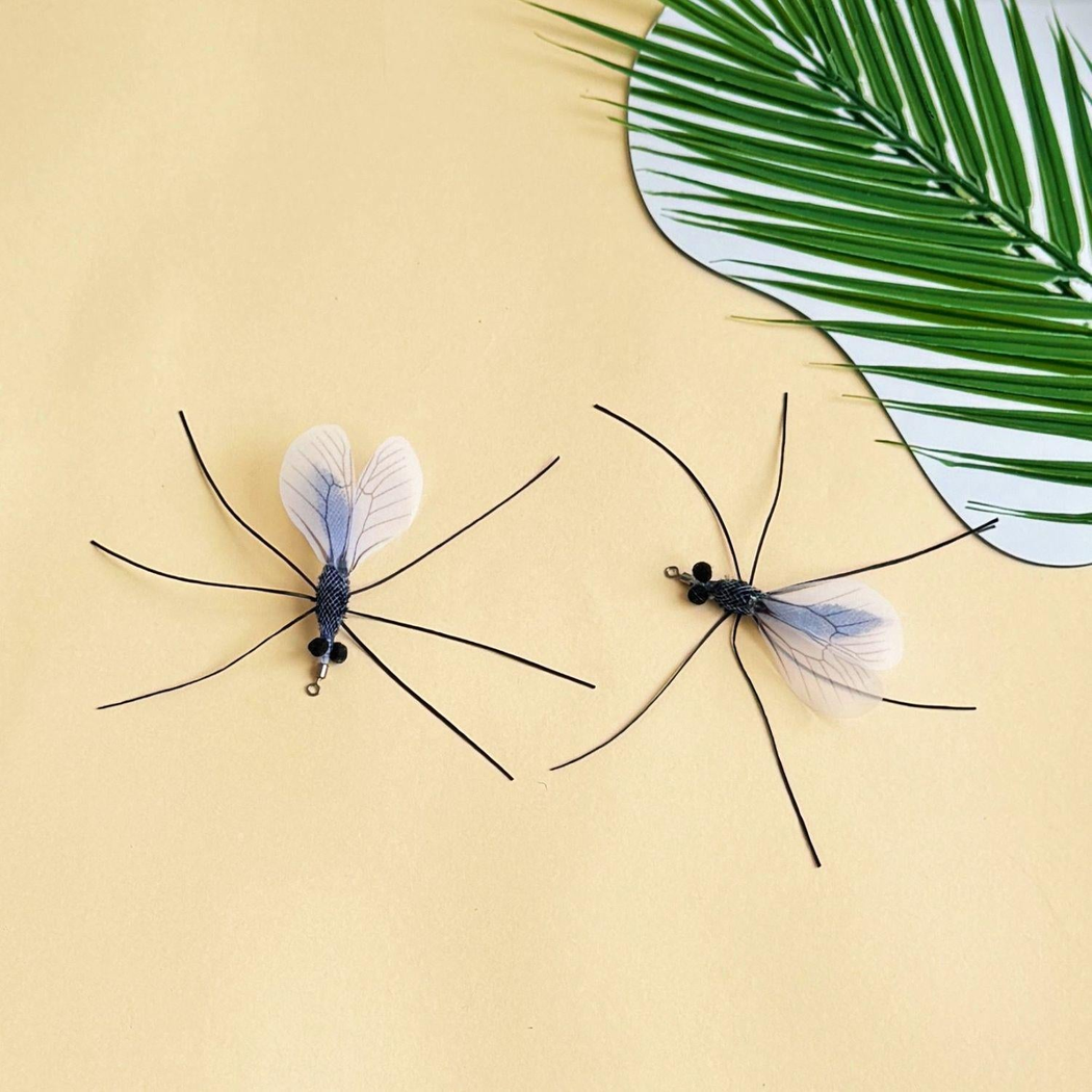 Two mosquito-shaped cat toy attachments arranged beside a palm leaf