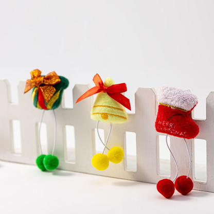 Gift, bell, and stocking pom-pom dangle cat toys arranged on a white fence