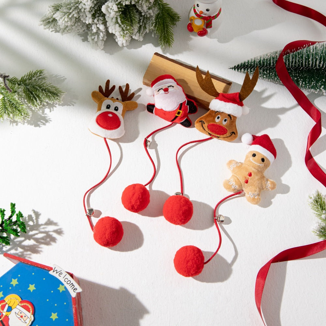 Four Christmas character pom-pom cat toys arranged with festive decorations