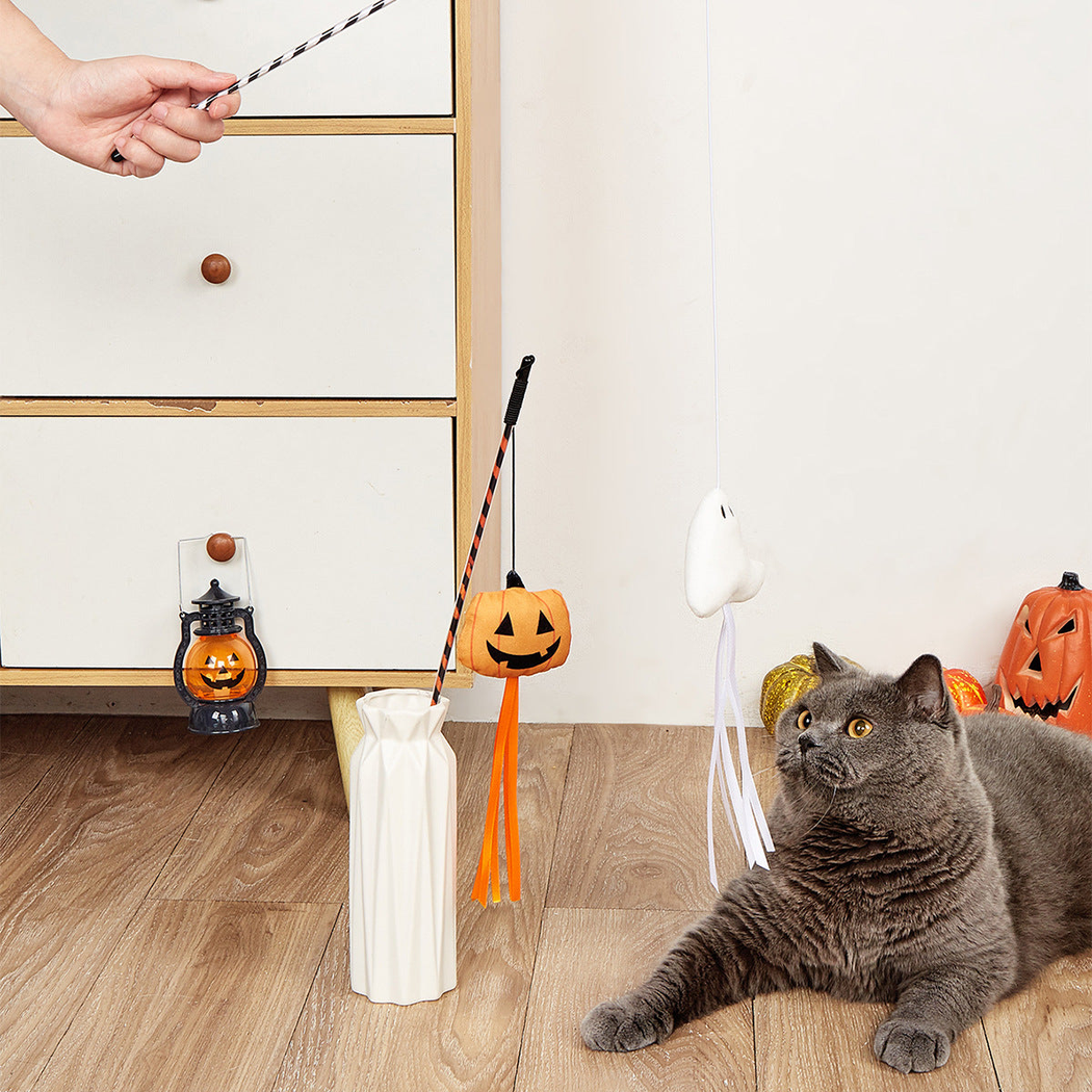 Cat watching white ghost and orange pumpkin wand toys in a Halloween setting