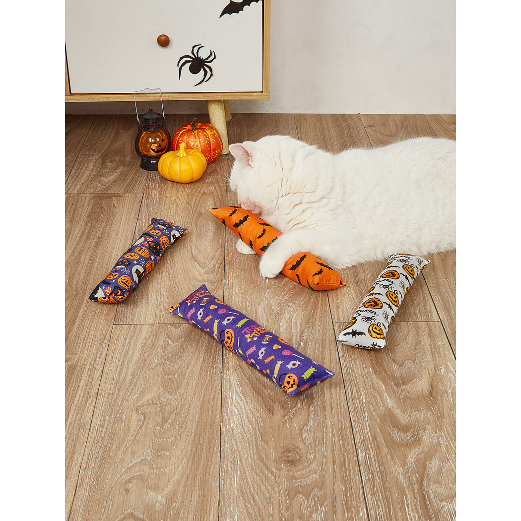 White cat holding an orange bat-print elongated cat toy in a Halloween setting