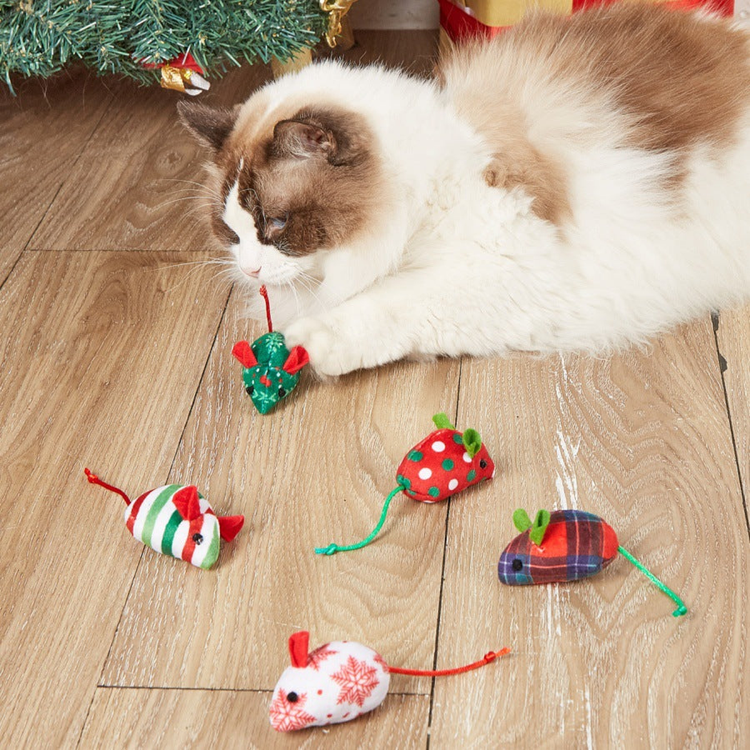 Cat playing with festive mouse-shaped toys beside a Christmas tree