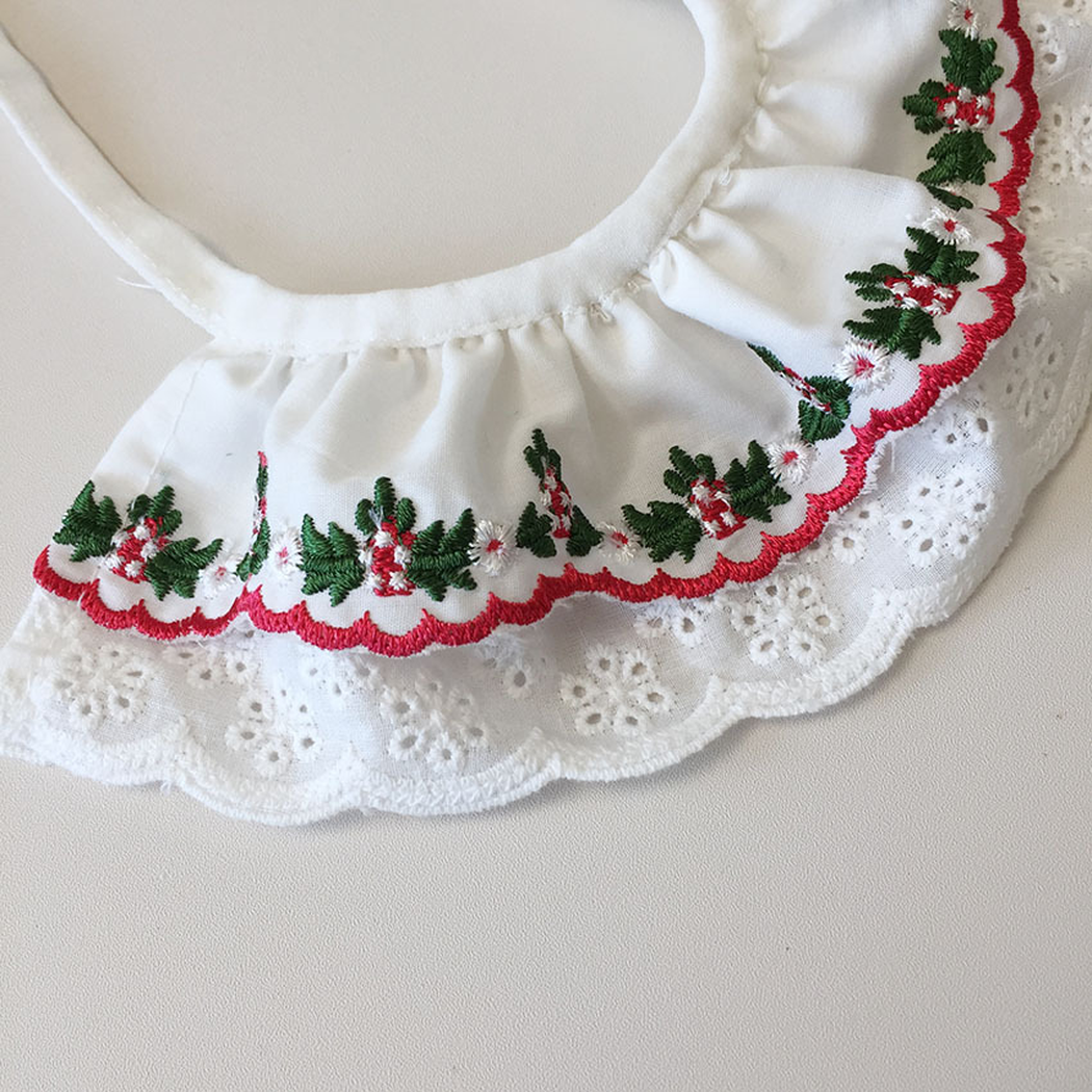 Close-up of green and red floral embroidery above scalloped white eyelet trim
