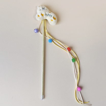 Cream cat teaser wand with fuzzy cat topper, ribbon streamers, pom-poms and bell