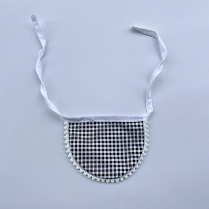Black gingham Pet Neckwear with white neck ties and pom-pom edging, laid flat.
