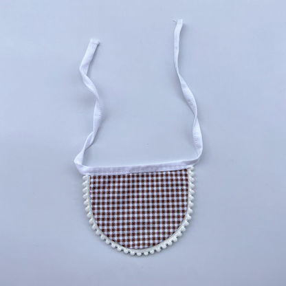 Brown gingham Pet Neckwear with white neck ties and pom-pom edging, laid flat.