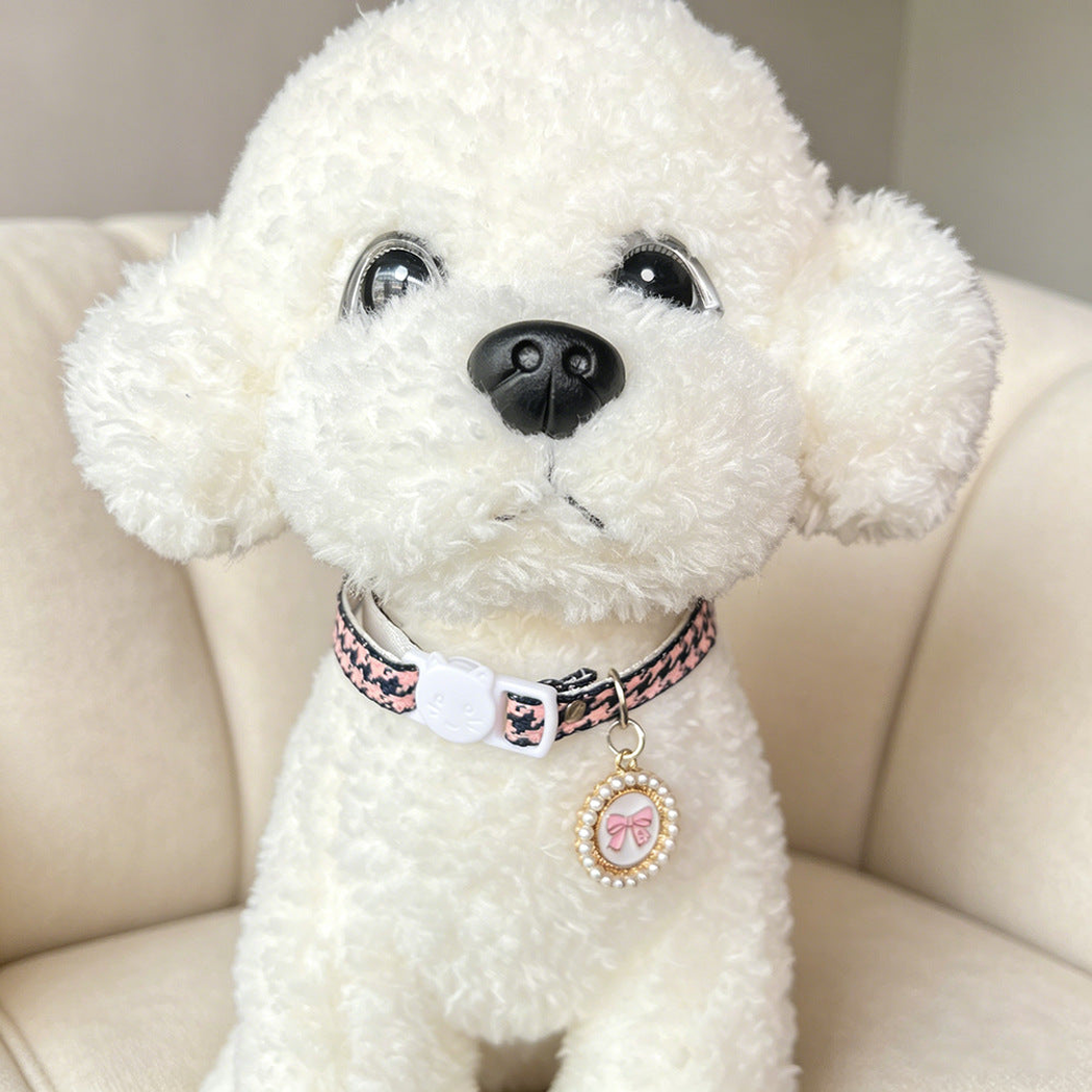 Pink houndstooth cat collar with bow charm worn by a white plush dog, close view