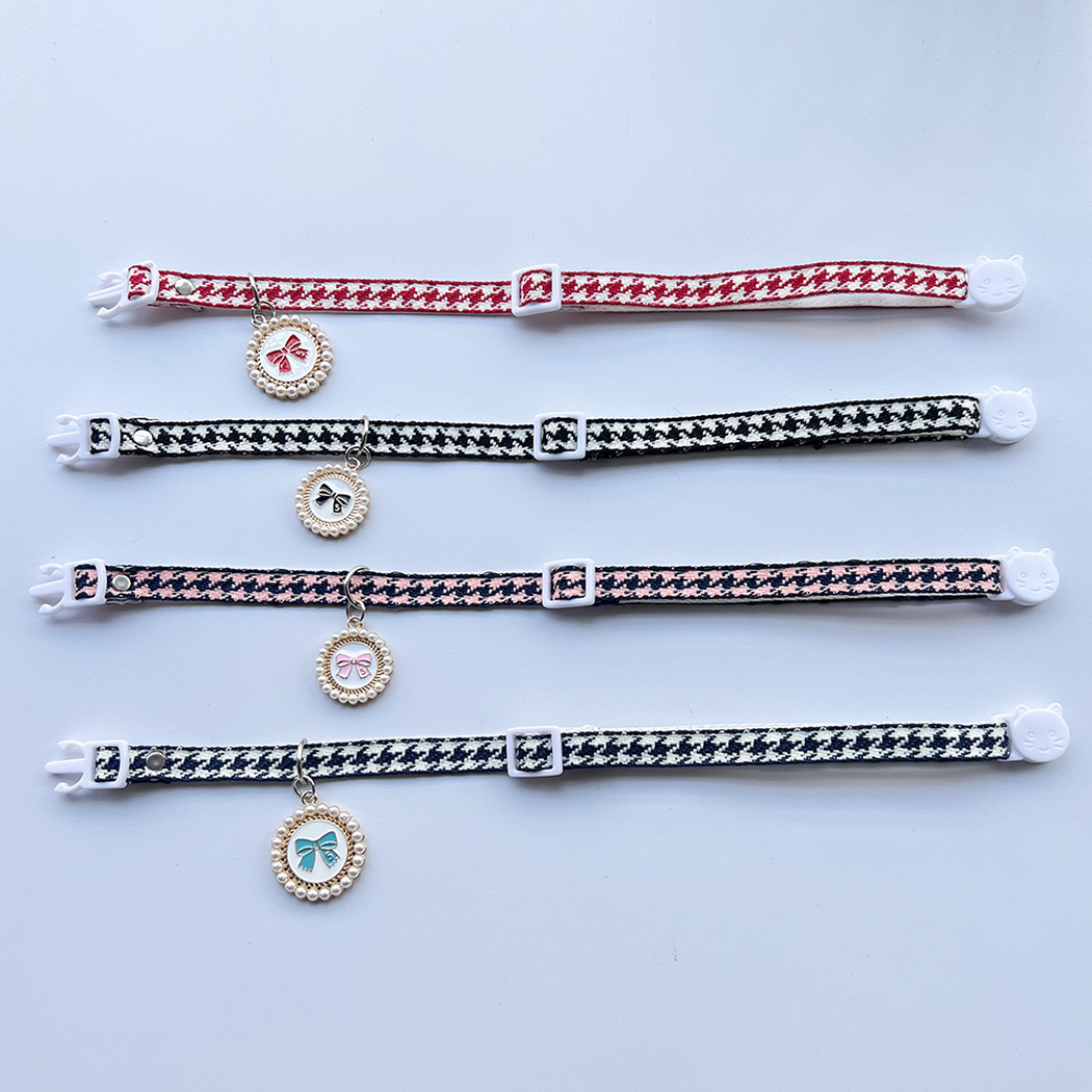 Four houndstooth cat collars laid flat to show adjustable straps and bow charms