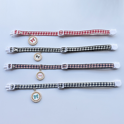 Four houndstooth cat collars laid flat to show adjustable straps and bow charms