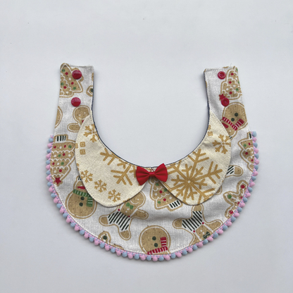 Light Bib pet neckwear laid open with red snap fasteners, snowflake lapels, a red bow, and pastel pom-pom trim.