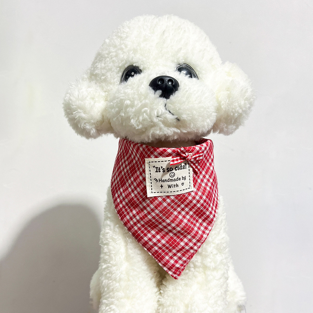 White plush dog wearing red checked bandana-style pet neckwear with a small bow and square label.