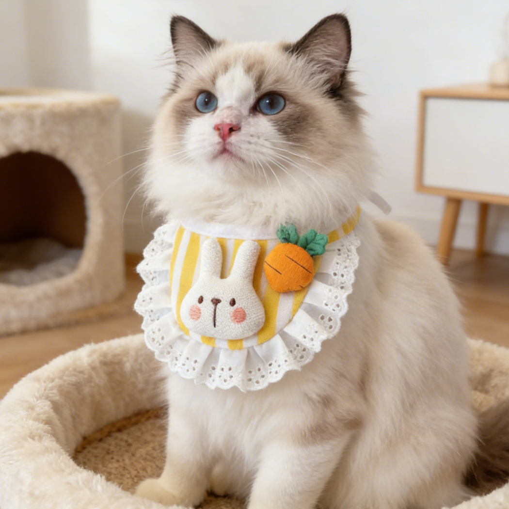 Long-haired cat wearing Yellow striped pet neckwear with rabbit and carrot decorations while sitting in a pet bed.