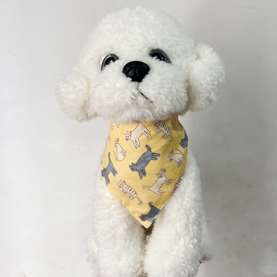 White plush dog wearing yellow cat-print pet neckwear with a single triangular front.