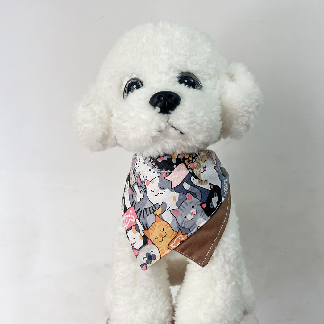 White plush dog wearing multicolor cat-print pet neckwear with overlapping points and a brown reverse.