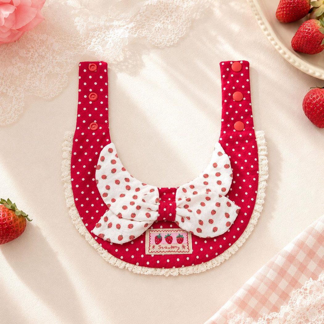 Red and white strawberry-patterned pet neckwear laid open to show both straps and rows of snap fasteners.