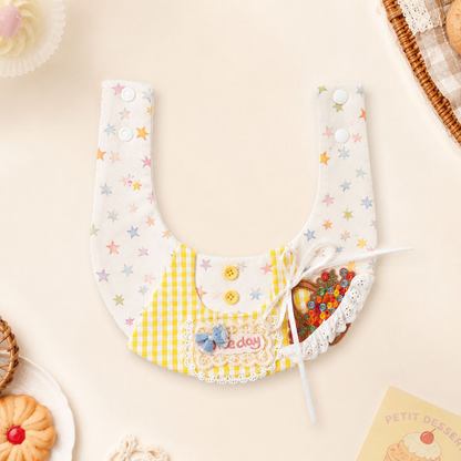 Yellow gingham and pastel star pet neckwear laid open among dessert props, showing extended neck straps and snap fasteners.