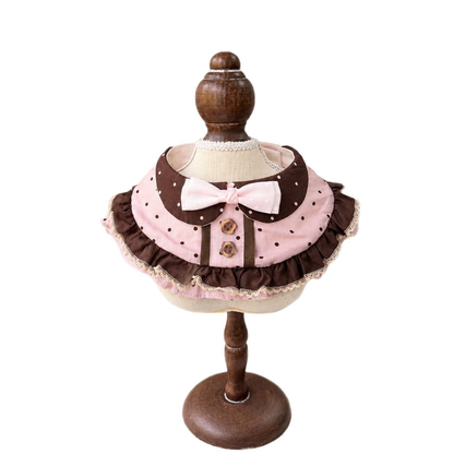 Pink and brown polka-dot pet neckwear with a front bow, decorative buttons, and layered ruffles on a display stand.