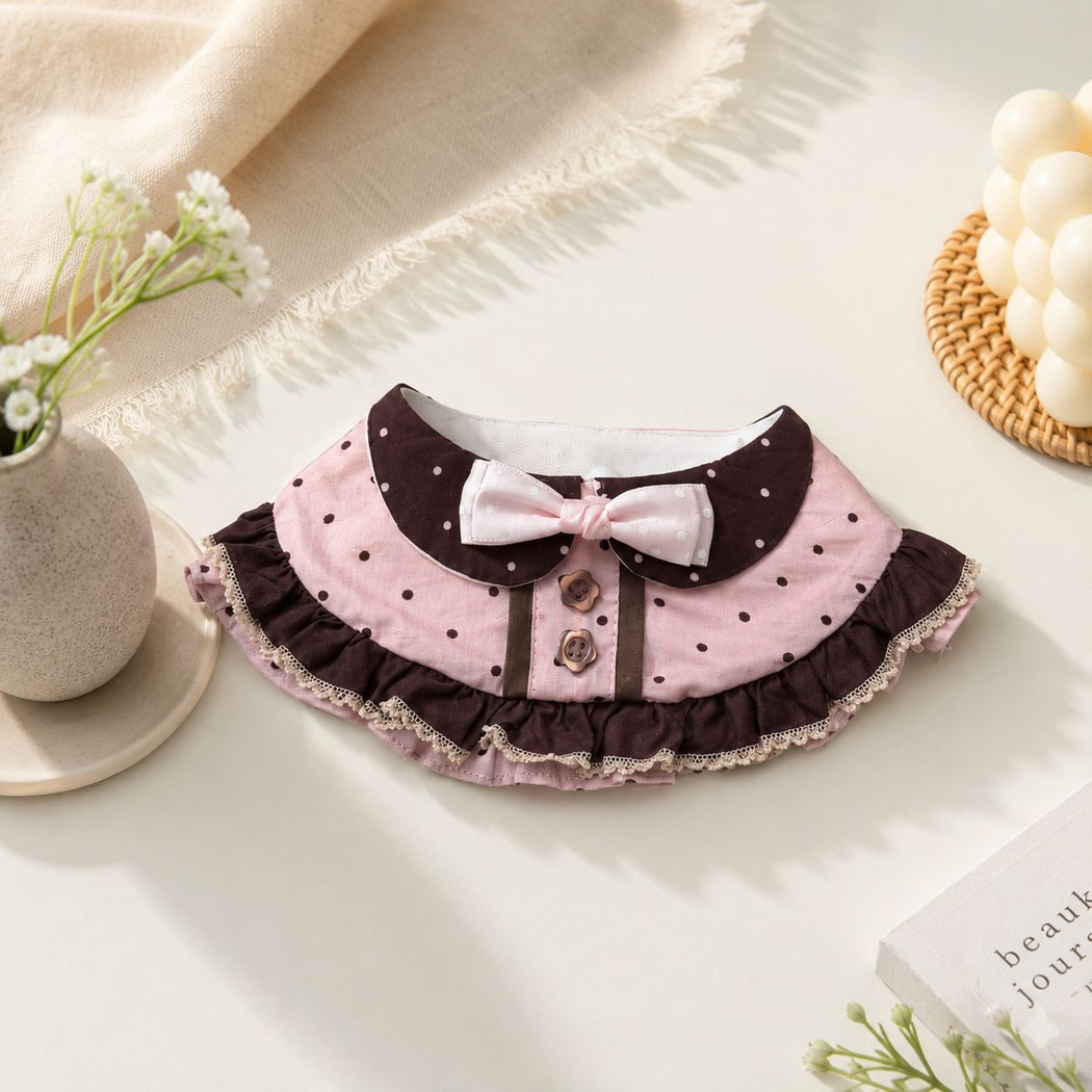 Pink and brown polka-dot pet neckwear with a bow and layered ruffles arranged on a tabletop.