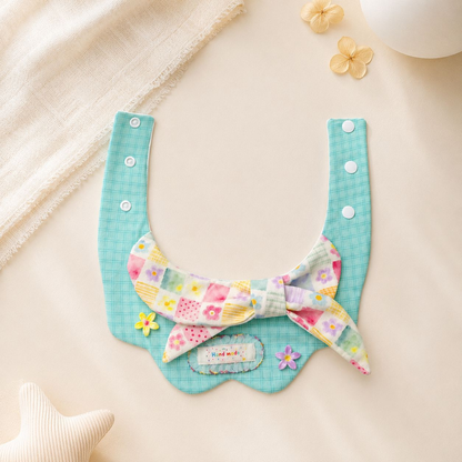 Mint plaid pet neckwear laid open, showing snap straps, a pastel floral bow and a scalloped bib panel.
