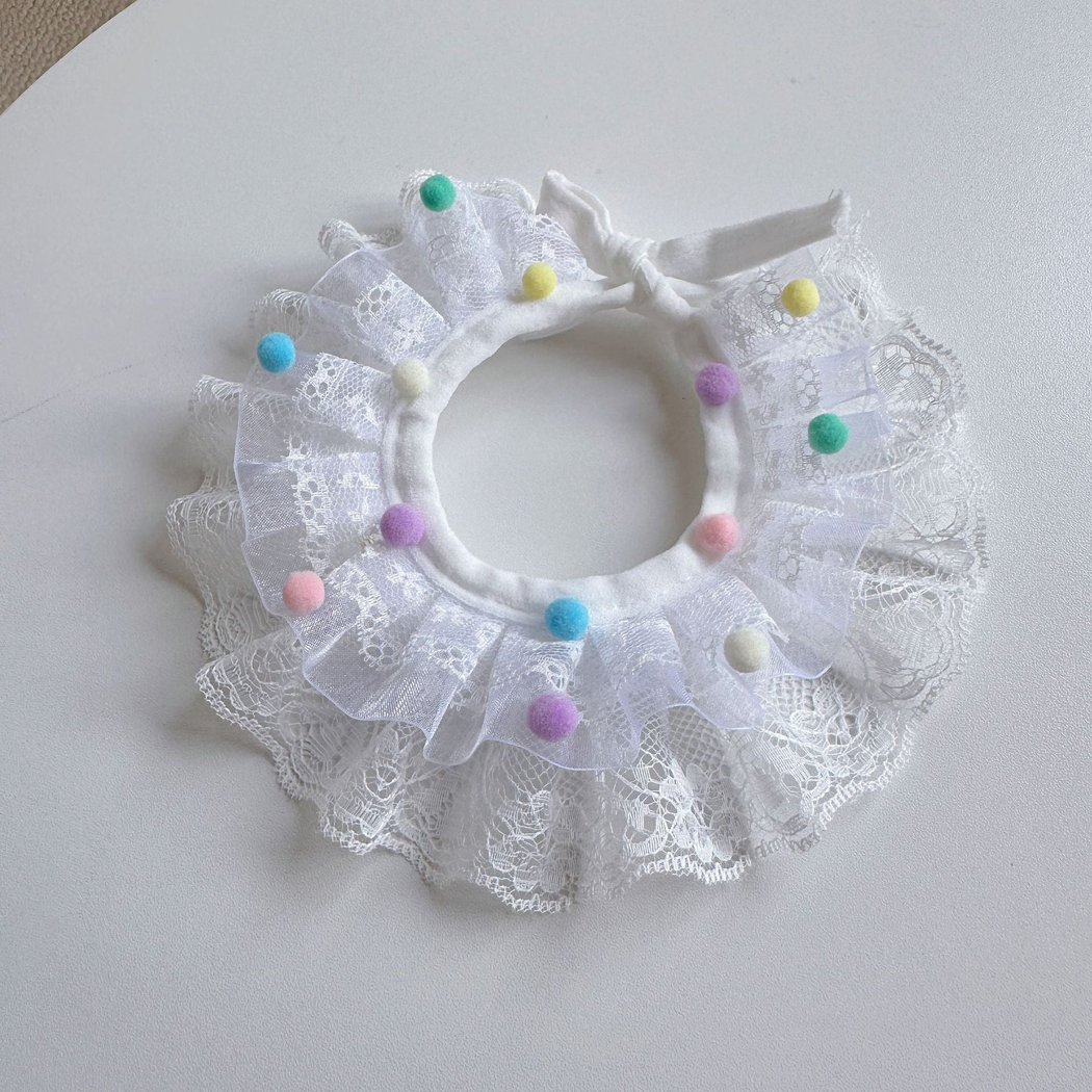 White pet neckwear with a ruffled bib, lace-like floral pattern, and multicolored pom-poms