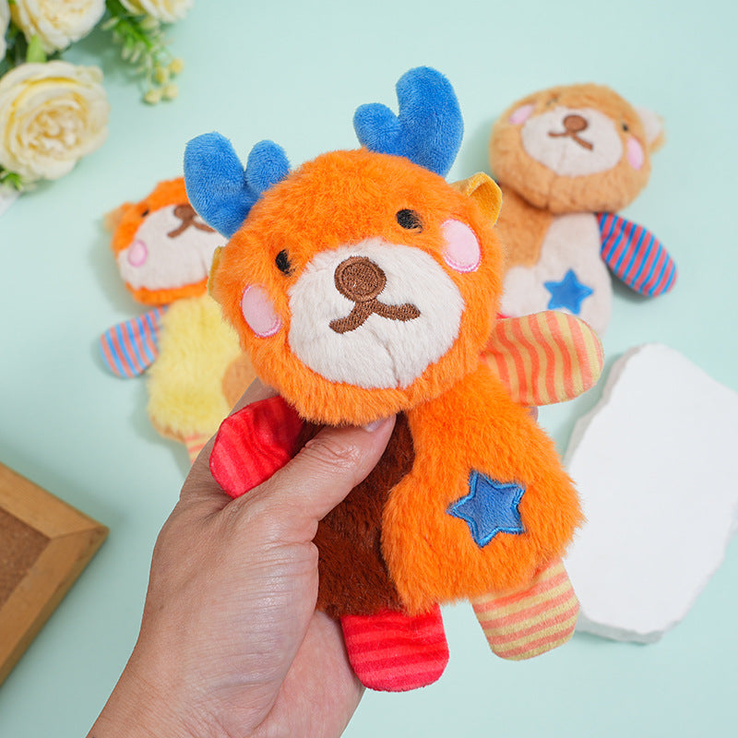 A hand holding an orange deer plush dog toy in front of other toys