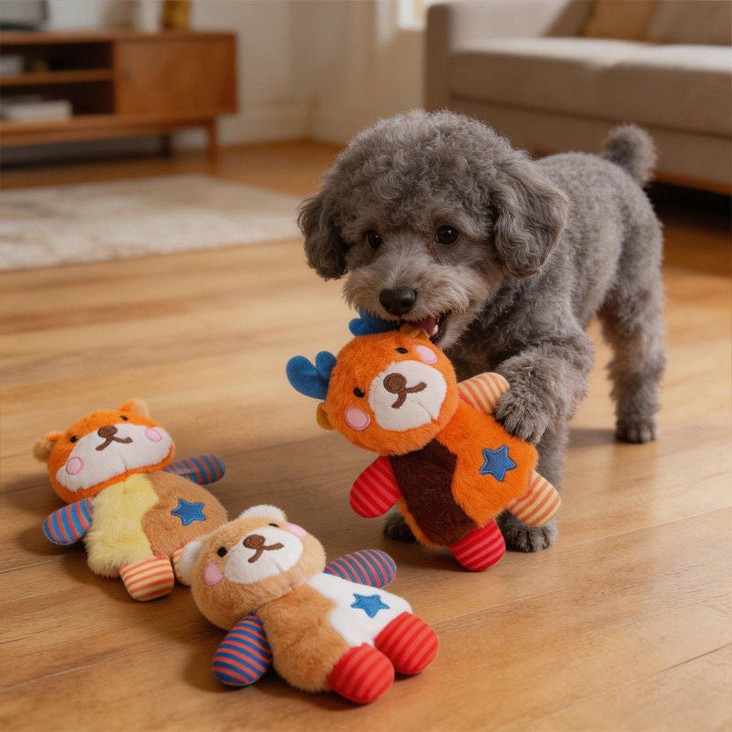 A gray dog holding an orange deer plush dog toy, with bear and fox toys on the floor